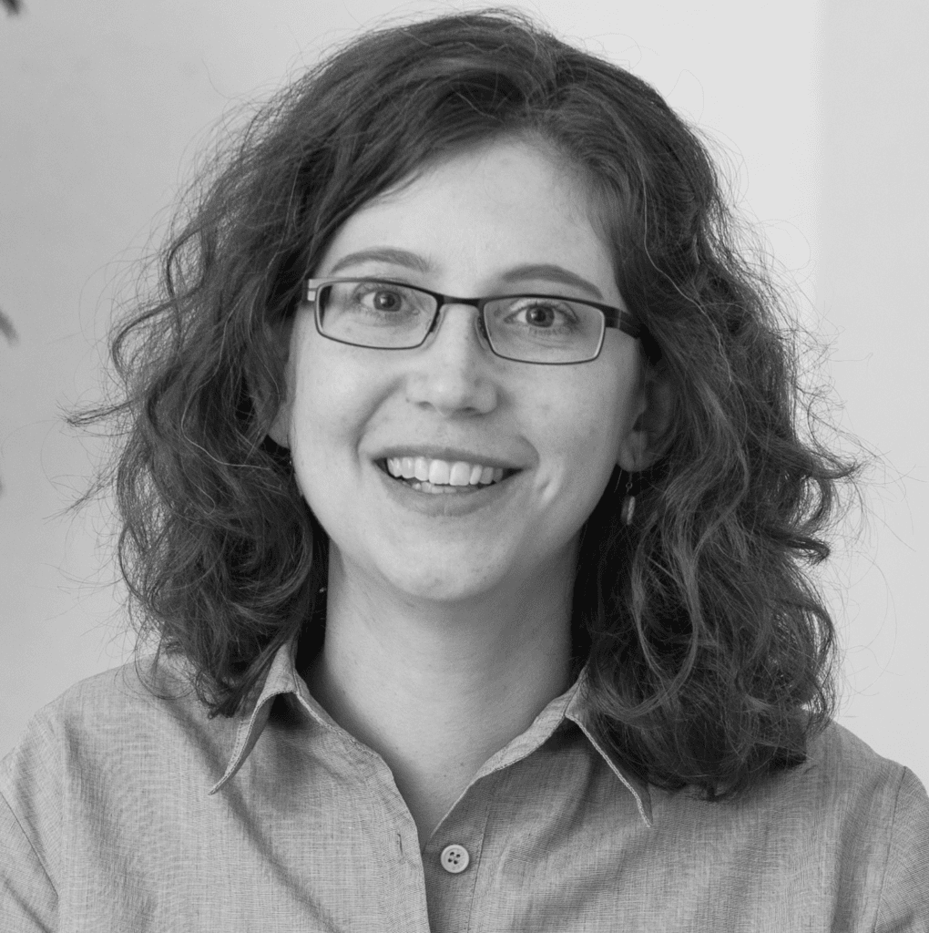 Black-and-white portrait of a smiling white woman with curly brown hair and glasses.